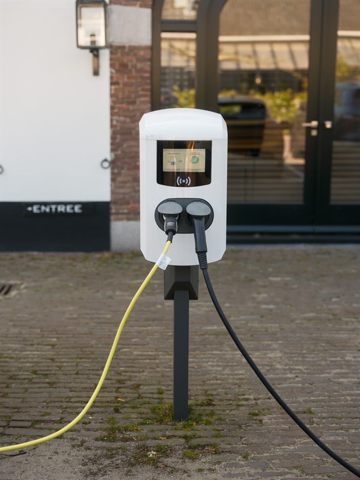 Laadpaal met twee aangesloten laadkabels op een geklinkerd voorterrein