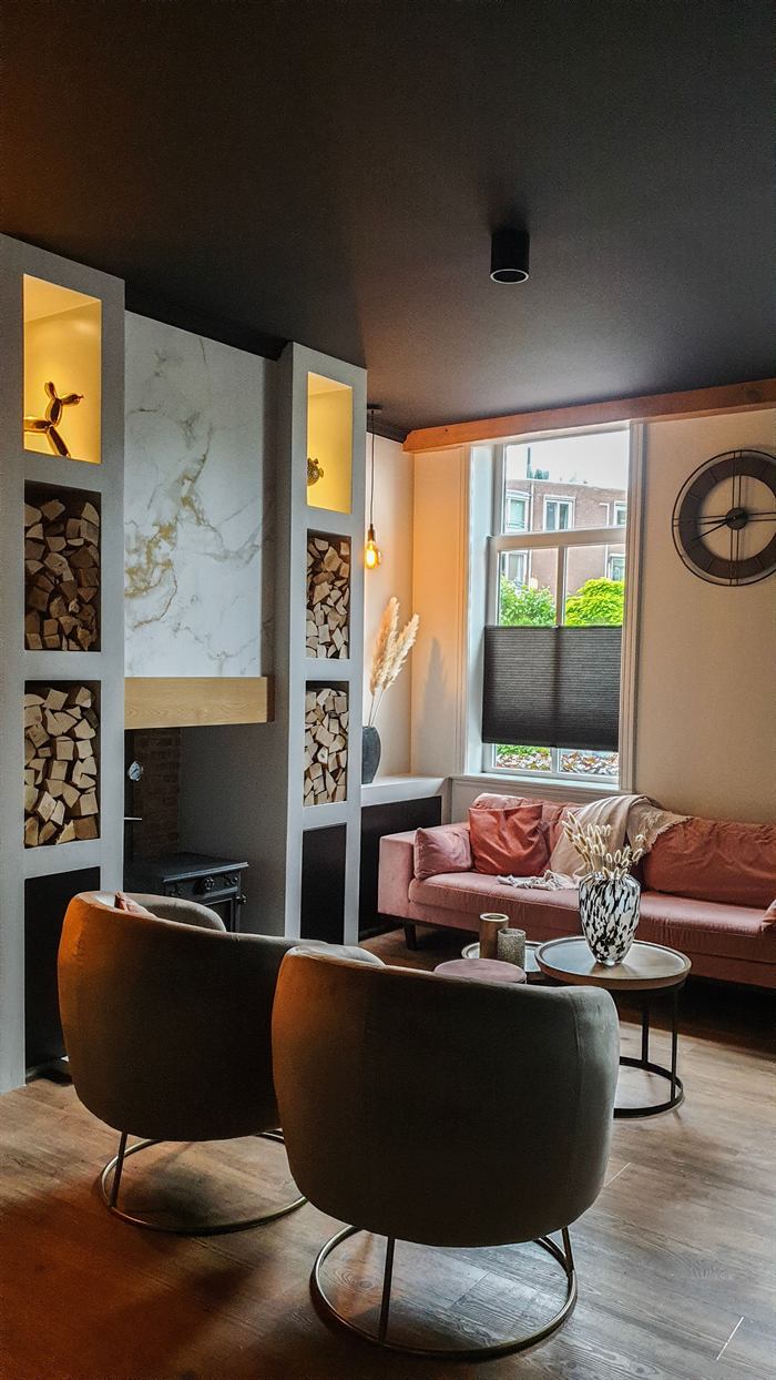 Woonkamer met maatwerk haardwand van marmer en nissen met haardhout
